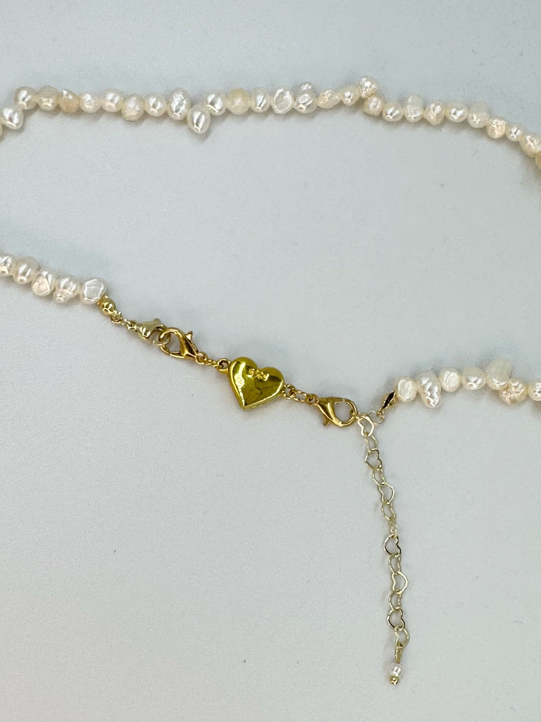 Armbånd med små hvide perler, guldfarvet hjerte-lås og sølvforlængelse med hjerteformede led.