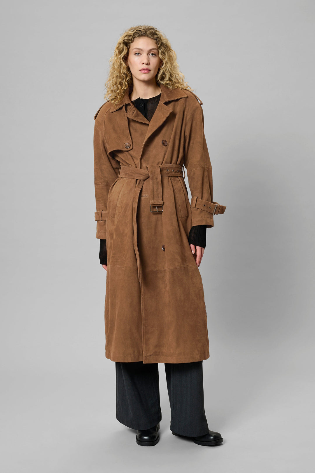 Kvinde iført cognacfarvet trenchcoat med bælte, epauletter og dobbeltknappet front.