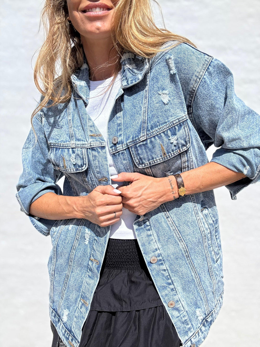 Kvinde iført lys denimjakke med knapper, brystlommer og opsmøgede ærmer. Løs pasform, casual stil.