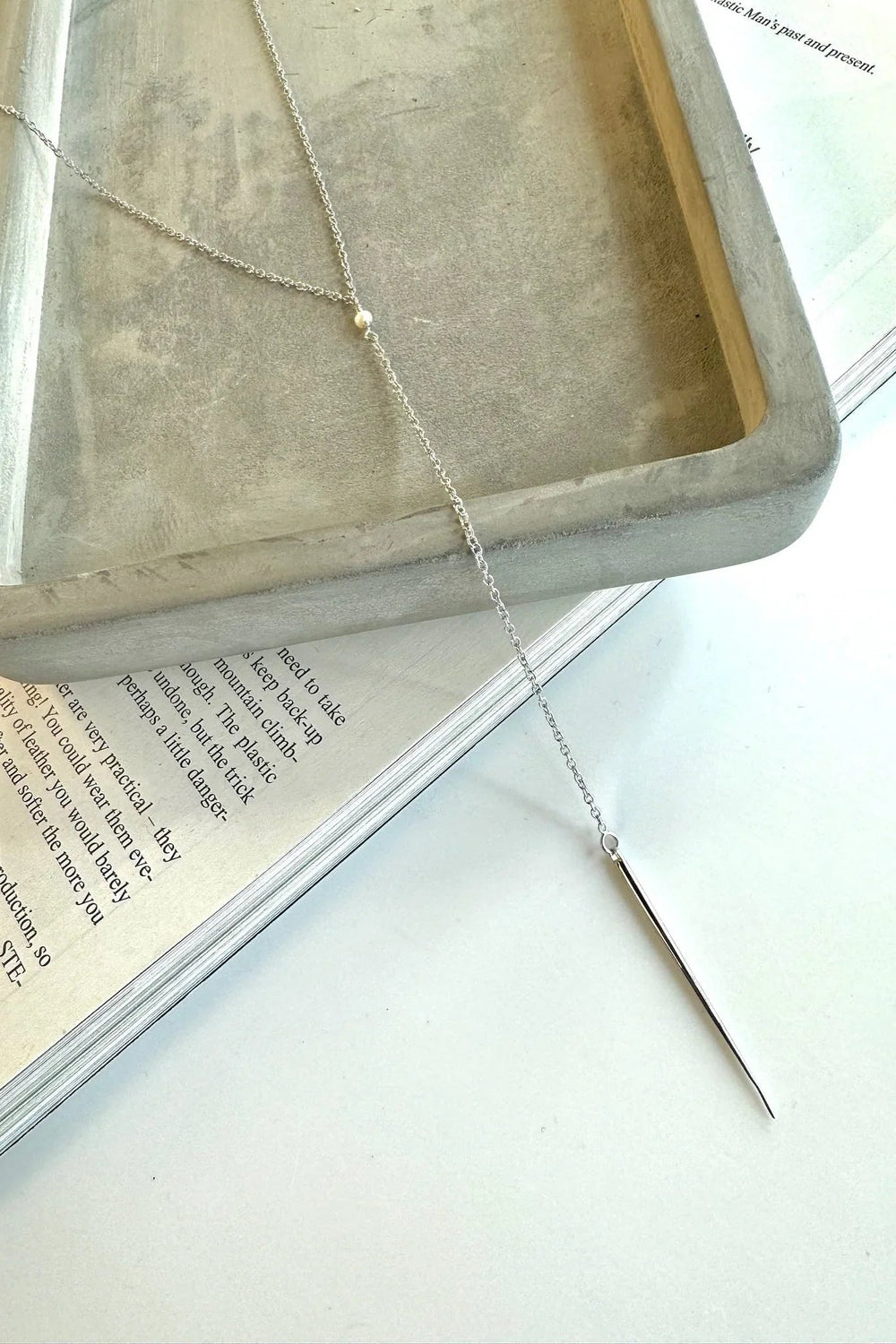 Halskæde i sterlingsølv med perle og spids, elegant præsenteret på en bog og bakke.