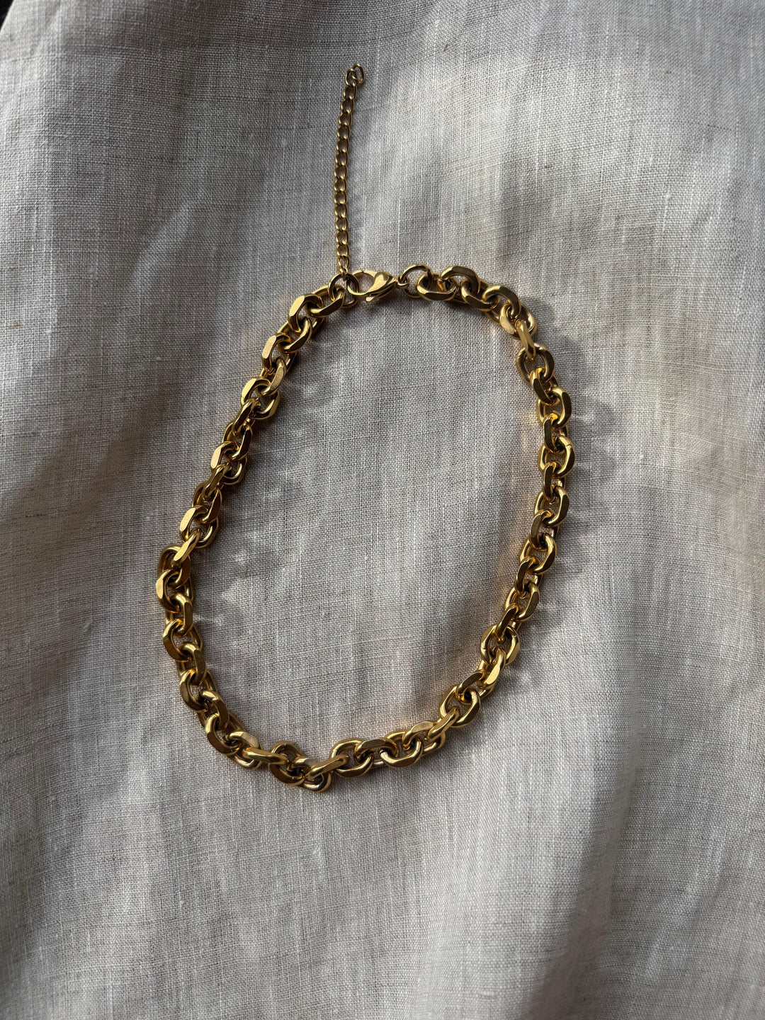 Chunky guldkæde med store led på lys stofbaggrund, skinnende overflade, alsidig som halskæde.