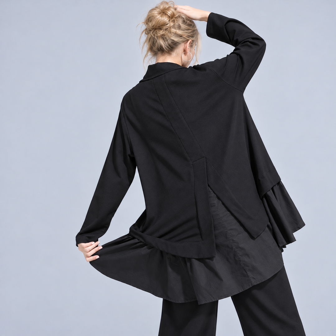 Berit bluse fra Sassy Copenhagen i sort med lange ærmer, halvhøj hals, løs A-formet pasform og asymmetriske flæser i lag langs underkanten på kvinde bagfra