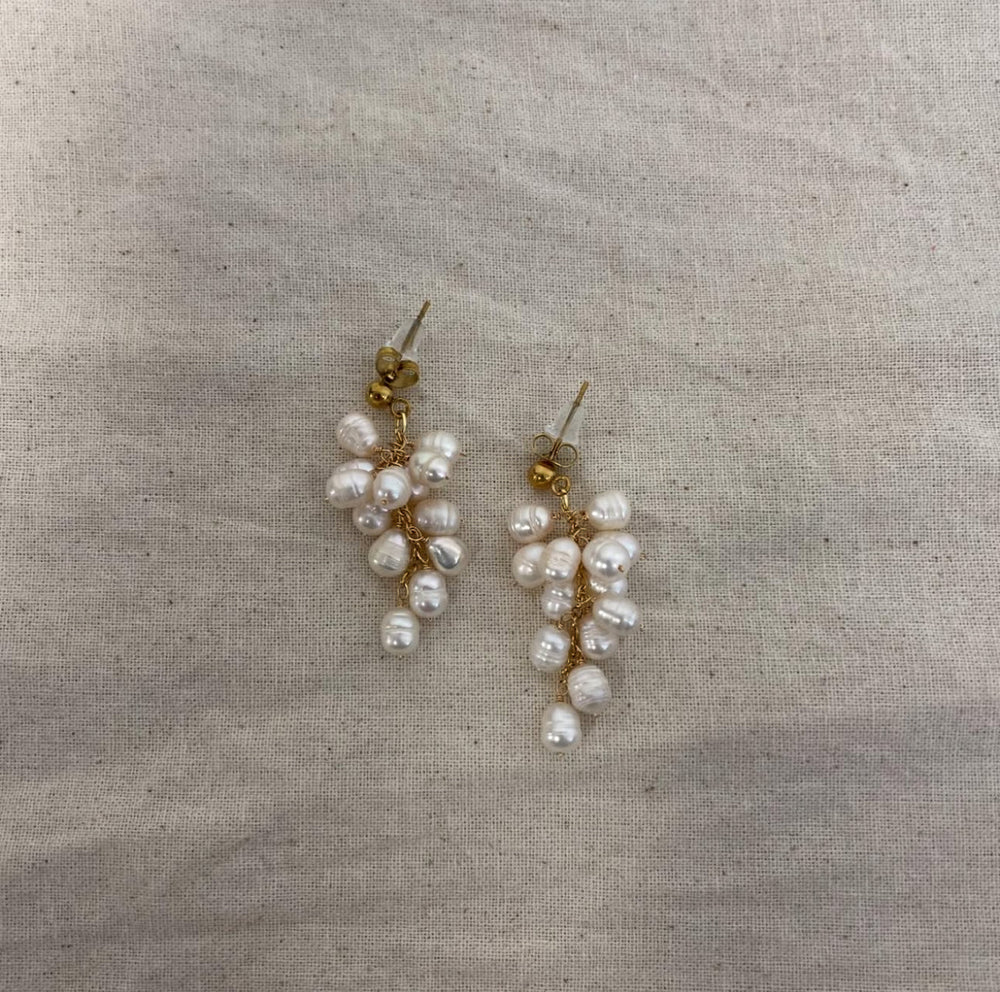 Øreringe med klynge af ferskvandsperler og guldfarvede metaldele på beige baggrund.