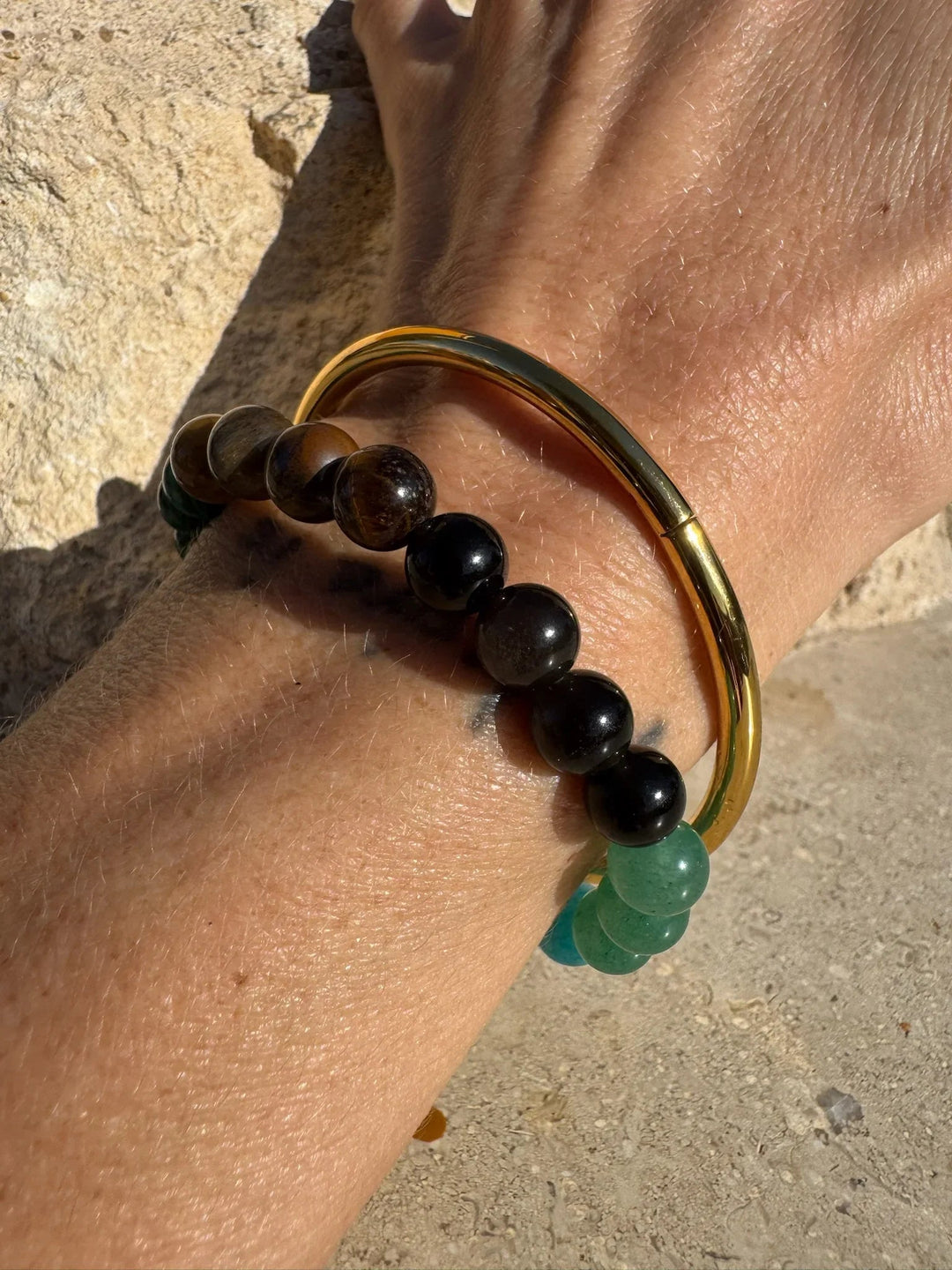 Håndled med to armbånd, et med grønne og sorte perler og et gyldent metalarmbånd.