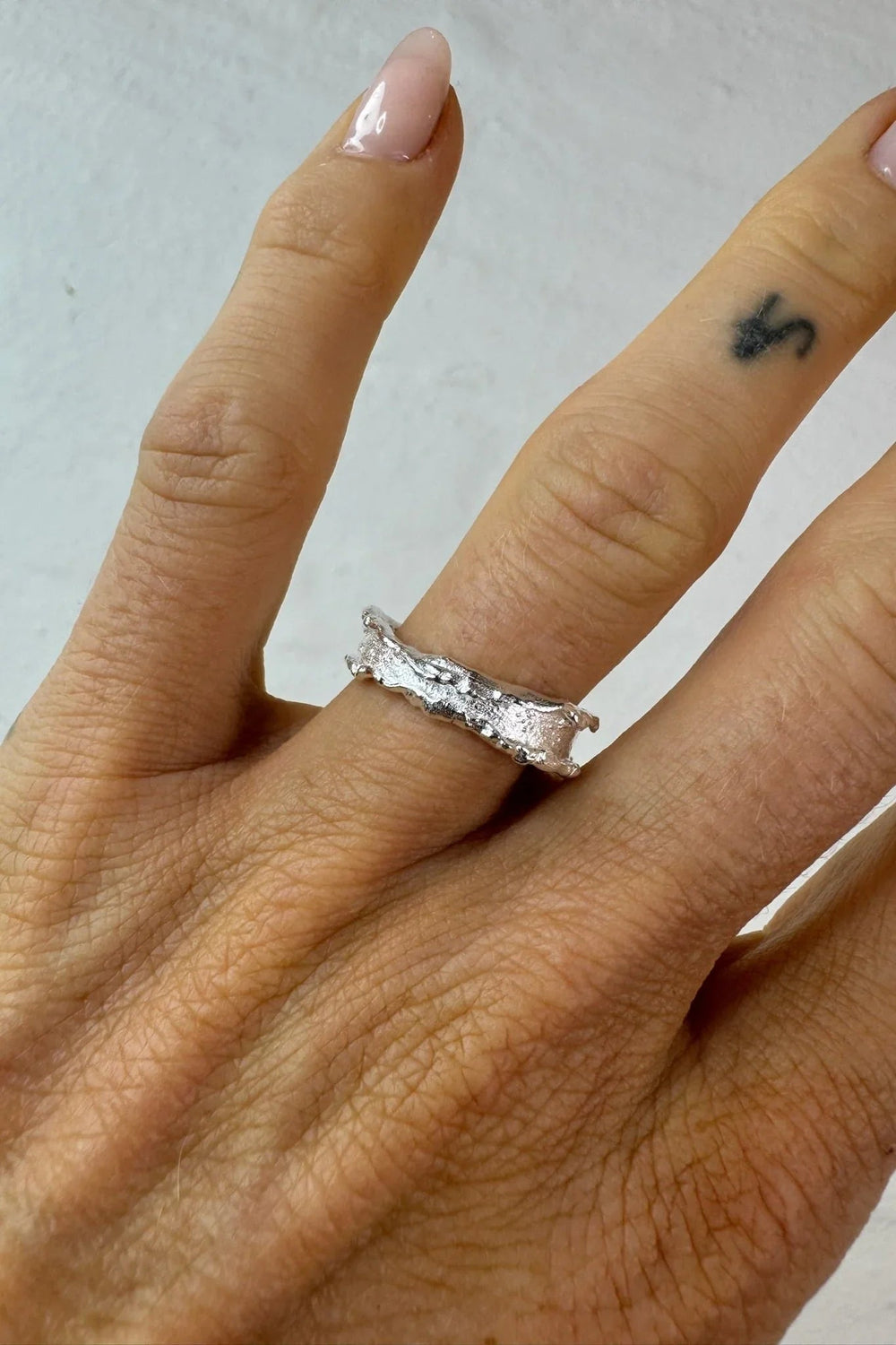 Hånd med en skinnende, tekstureret ring i 925 sterlingsølv med en ru overflade.