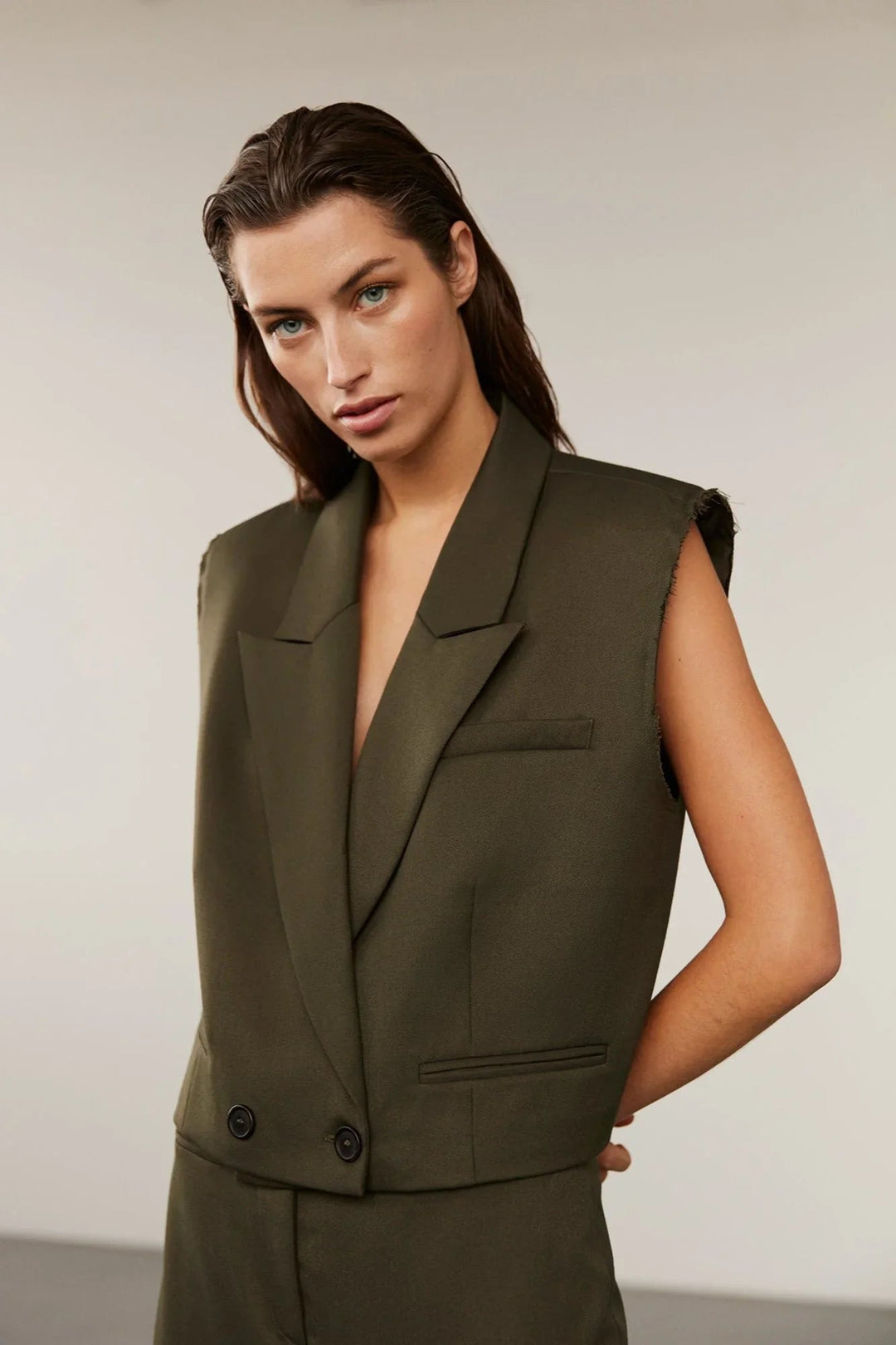 Olivengrøn vest med klassisk krave, dobbeltknaplukning og rå kantdetaljer på skuldrene.
