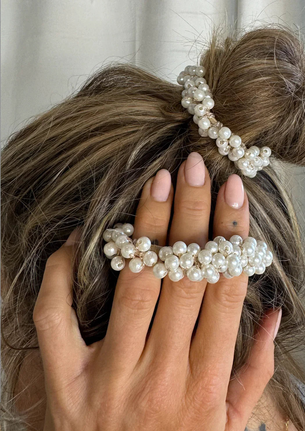Hår i knold med perle-elastik. Hånd med matchende perle-armbånd hviler på hovedet. Elegant look.