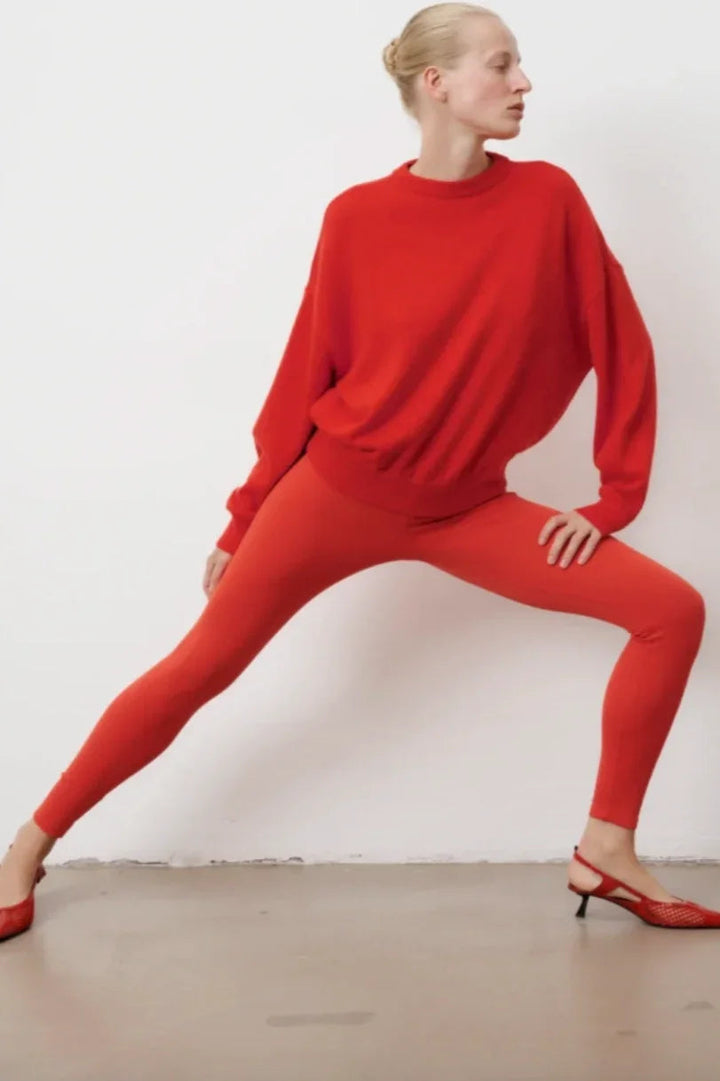 Person i orange leggings og stor sweater, poserer dynamisk. Leggings er højtaljede og ankellange.