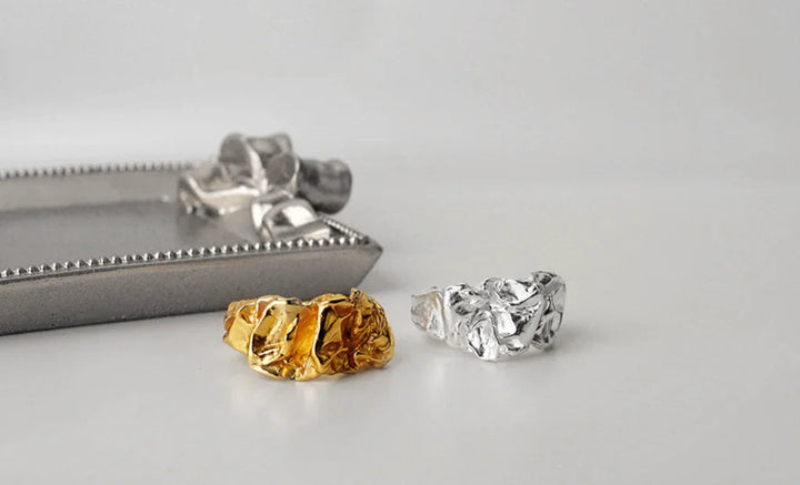 Arlinda ring fra Andcopenhagen i 18 karat guldbelagt og 925 sterlingsølv vist ved siden af et dekorativt fad.