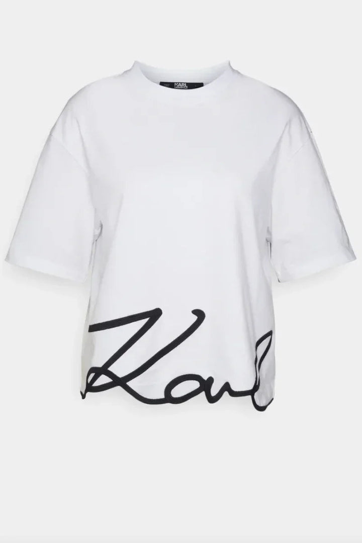 Hvid T-shirt med rund hals og sort, kursiv signatur på kanten.