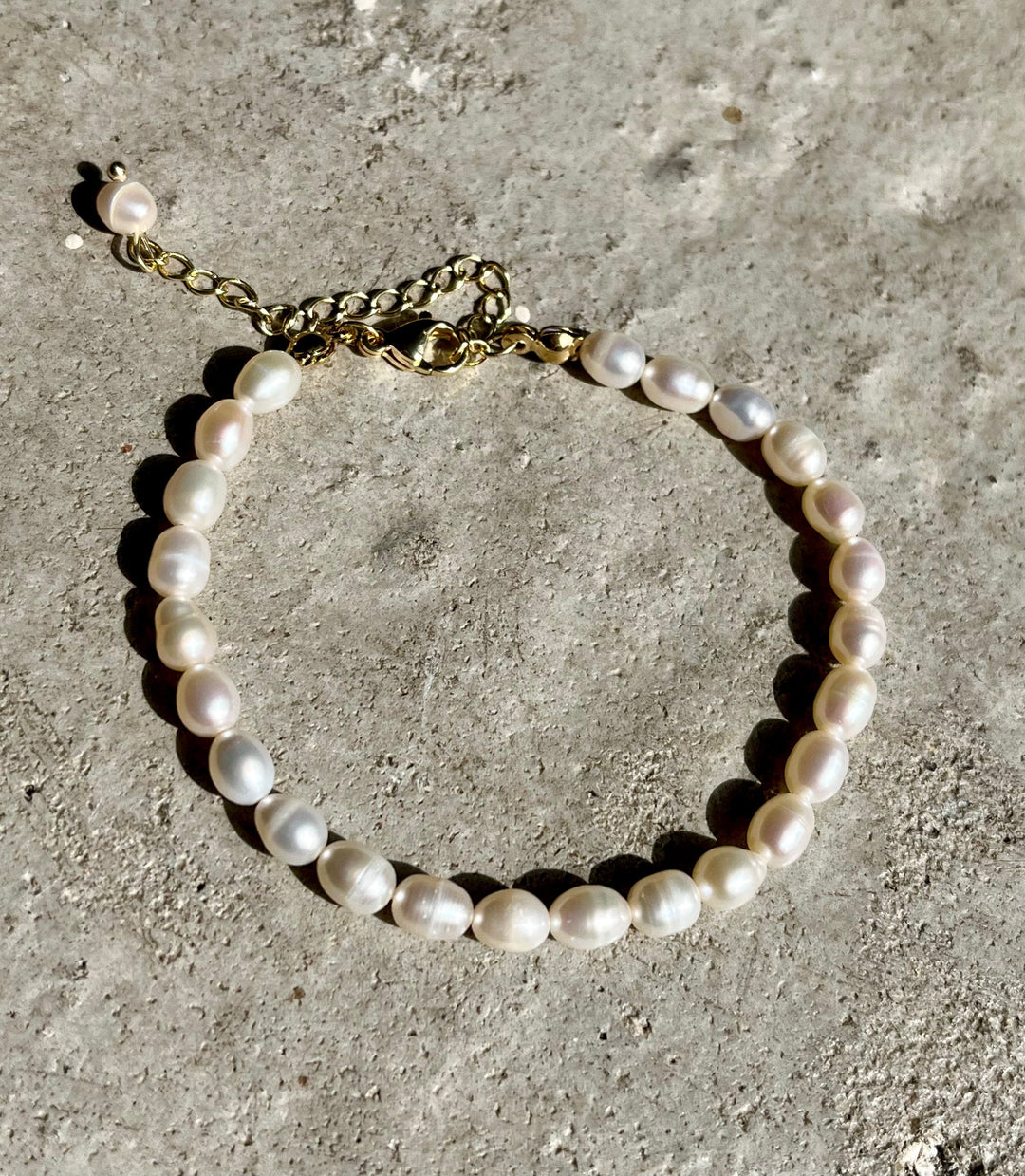 Armbånd med ovale perler i hvide og pastelfarver på en ru overflade. 18 karat guldbelagt kæde.