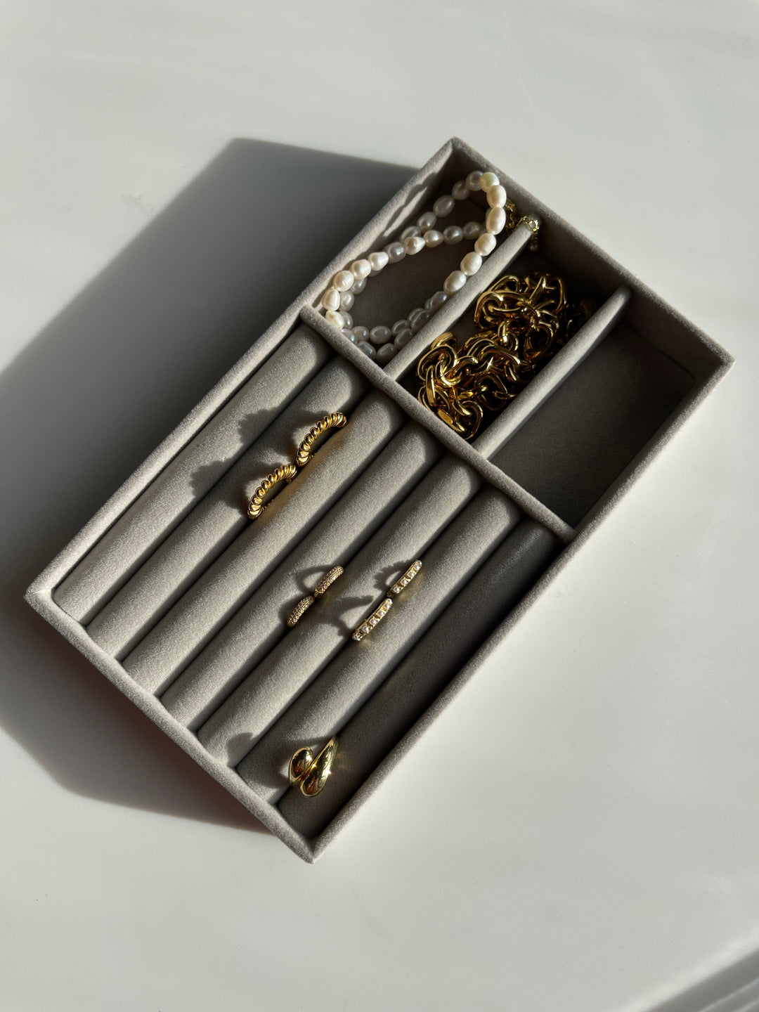 Smykkeorganisator med velour, indeholder ringe, perlearmbånd og guldkæder i separate rum.