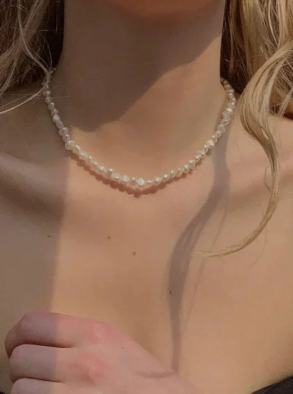 Halskæde af små, hvide perler om halsen på en person, elegant og delikat stil.