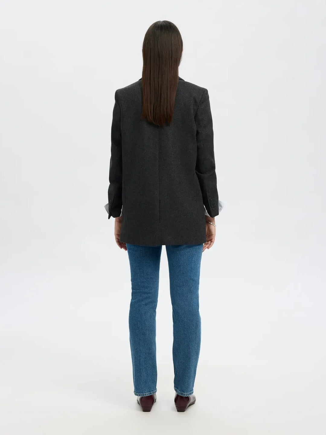 Bagside af person i sort blazer, blå jeans og brune sko. Blazeren har et subtilt mønster.