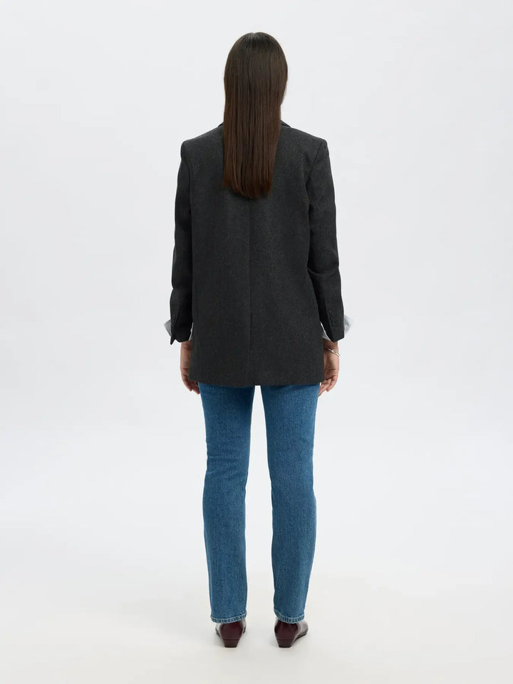 Bagside af person i sort blazer, blå jeans og brune sko. Blazeren har et subtilt mønster.