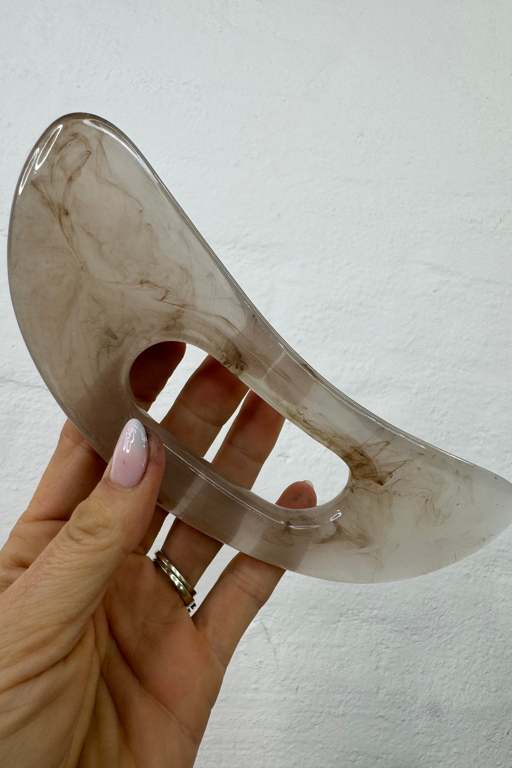 Hånd holder Andcopenhagen Basics Gua sha værktøj til kroppen – Cana, lavet af glat sten.