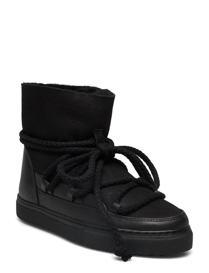 Sort vinterstøvle med højt skaft, tykke snørebånd og flad, mønstret sål. Mærke "INUIKII" synligt.