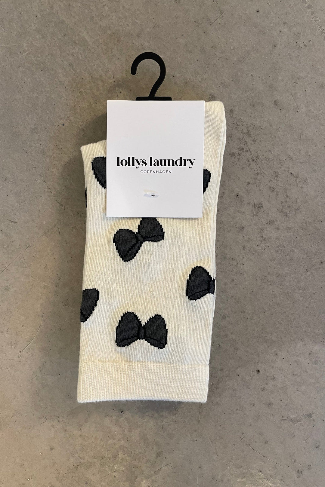 Lollys Laundry BowLL Socks in creme color with black bow pattern, made of cotton blend, shown folded with packaging on a hang