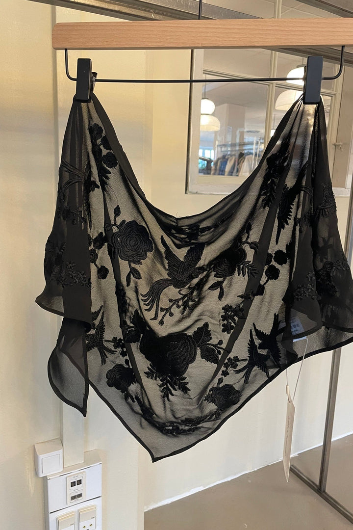 Lollys Laundry ElianaLL Triangle Scarf in black, featuring an embroidered floral pattern, displayed hanging on a hanger.
