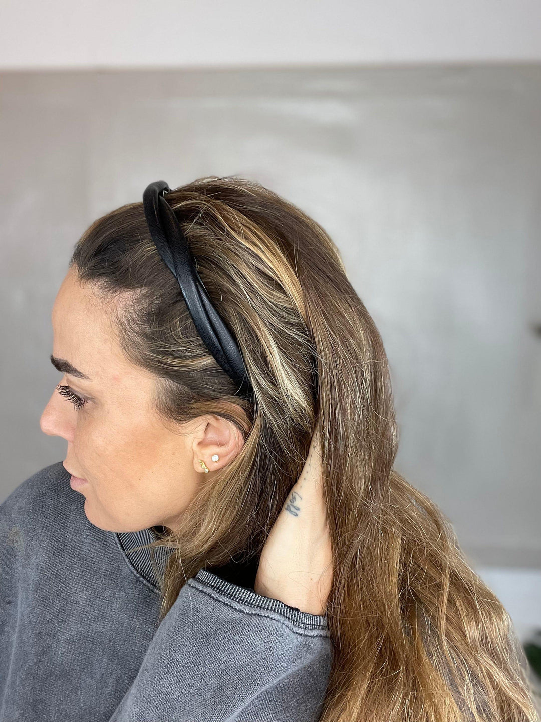 En person med sort, smal læderhårbøjle indendørs, iført grå trøje og har langt hår.